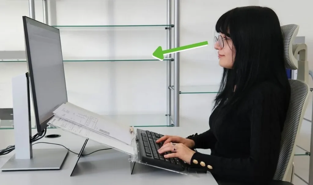 Oseba sedi vzravnano in naslonjeno na stol za računalnikom, medtem ko zelena puščica označuje pravilno višino pogleda proti zaslonu in ergonomsko ureditev delovnega mesta.